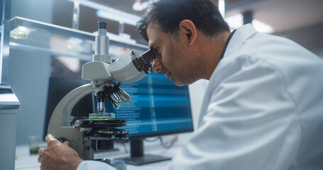 Molecular Biology Research Scientist Looking at a DNA Sample Under a Microscope in an Applied Science Laboratory. Portrait of an Adult Lab Engineer in White Coat Working on Vaccine and Medicine