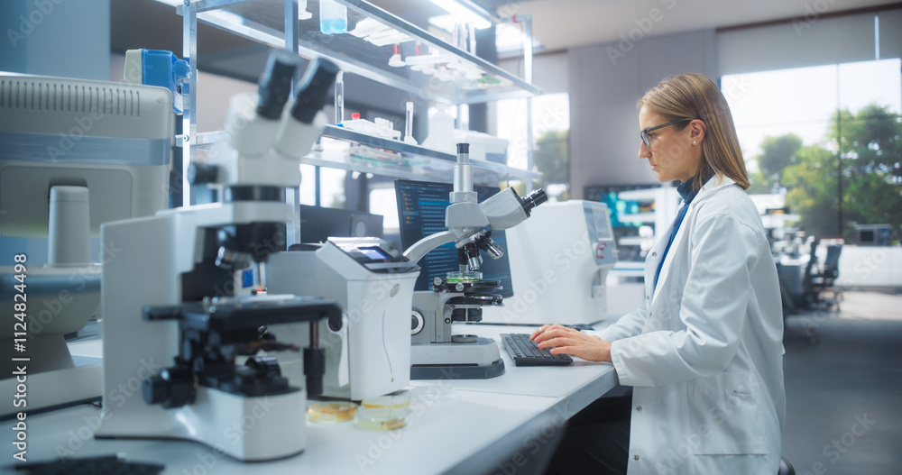 Poster Medical Research and Development Laboratory: Beautiful Caucasian Female Scientist Working on a Computer and Looking at a Petri Dish Sample Under a Microscope. Advanced Biotechnology Lab