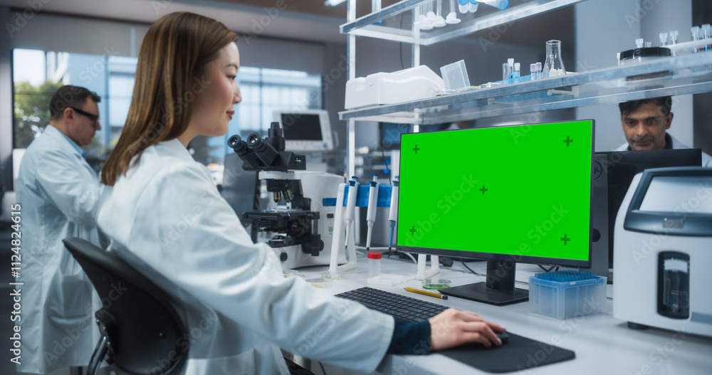 Poster asian female scientist working on a desktop computer with a green screen chroma key mock up display.