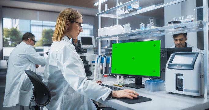 Caucasian Female Scientist Working on a Desktop Computer with a Green Screen Mock Up Display. Advanced Biotechnology Laboratory in a Medical Research and Development Center