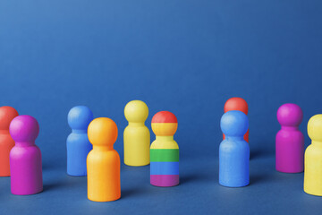 One wooden figure in LGBT colors among others on blue background. Tolerance and acceptance