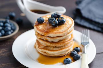 Buttermilk pancakes with blueberries and maple syrup on white plate, closeup view