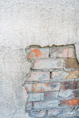 A close-up view of a cracked plaster wall revealing the underlying brick structure. The exposed bricks and worn surface textures create an industrial and weathered aesthetic. Ideal for design themes