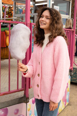 A young curly hair brunette smiles and holds fluffy cotton candy on a stick. Amusement park...