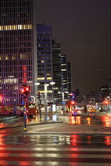 Urban night street with reflections of traffic lights on wet pavement, surrounded by modern city...