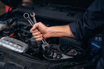Tools in hand. Close up view of mechanic in car service station