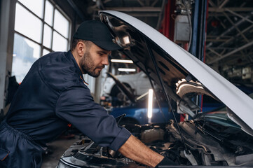 View from the side, opened hood. Mechanic working in a car service station
