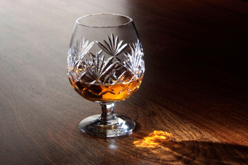Glass of cognac on a wooden table background with alight reflection.