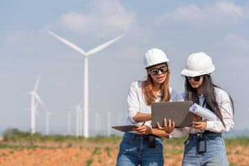 Two women are looking at a laptop in a field with windmills in the background