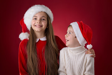 Happy girl and boy siblings in Santa hats, smiling and celebrating the festive Christmas season with warmth and happiness on portrait on red background