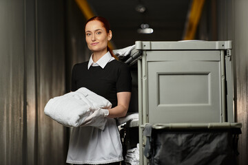 Beautiful woman skillfully arranges clean linens while managing a busy laundry cart.