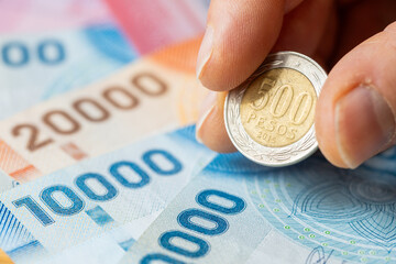 Chile money. 500 pesos coin held in fingers. Banknotes lying on the table. Business concept....
