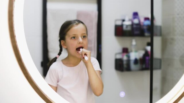 Portrait of young Caucasian girl with missing teeth brushing teeth while looking in bathroom mirror, emphasizing good oral hygiene habits.