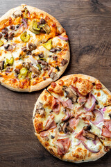 Two freshly baked pizzas on a wooden table. One features a topping of yellow peppers and mushrooms, while the other is topped with ham and red onions. Perfect for food enthusiasts.