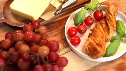 Vibrant Mediterranean brunch plate with fresh cherry tomatoes, juicy grapes, aromatic basil, and golden artisan bread twist, complemented by cheese, embodying fresh, nourishing flavors.