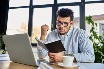 Handsome man in glasses reading from a notebook at a stylish workspace with plants around him.