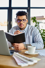 Young man with glasses engrossed in writing notes, surrounded by plants and natural light
