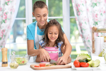 Cute little brother and sister preparing salad together at kitchen