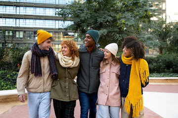 Front view of happy multiethnic college student friends laughing embracing together walking around city on a winter day.