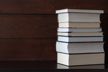 Stack of books on shelf against  wooden wall background.