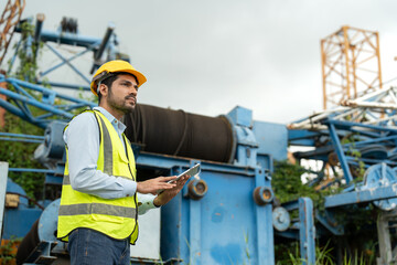 Confident construction male crane operator wearing a yellow hard hat and safety vest with tablet...