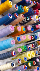 Close-up of colorful thread spools on a wall-mounted rack in a sewing studio. Perfect for...