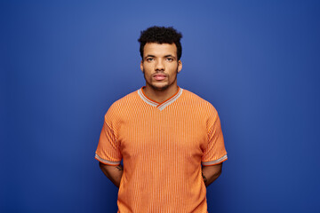 Confident individual with distinct style poses against a bold blue wall in an orange outfit.