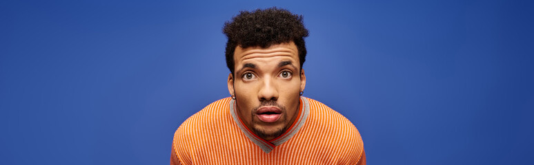 A handsome man poses thoughtfully against a bright blue backdrop, radiating charm.