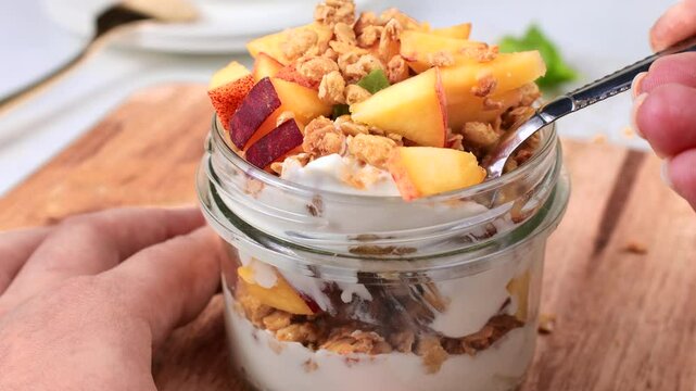 Eating homemade peach and yogurt parfait jar with fresh peaches with a spoon close up