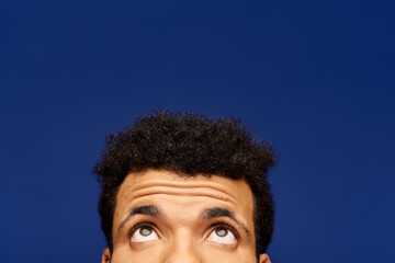 A handsome man looks thoughtfully upwards, his expression hinting at curiosity and wonder.
