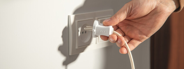 Hand holding electric plug into a power outlet.