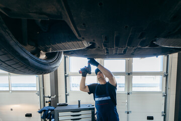 Young car mechanic at repair service station inspecting car wheel and suspension detail of lifted...