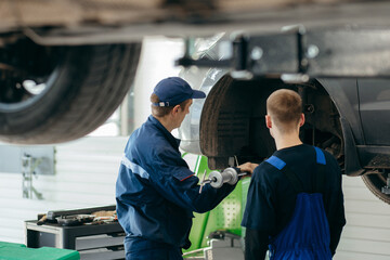 Young car mechanics at repair service station inspecting car wheel and suspension detail of lifted...