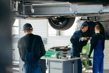 Young car mechanics at repair service station inspecting car wheel and suspension detail of lifted automobile