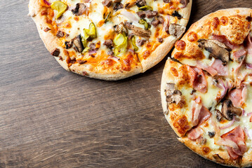 Two delicious pizzas on a wooden table. One topped with mushrooms, peppers, and meats, and the other featuring ham and cheese. Perfect for sharing or a casual meal.