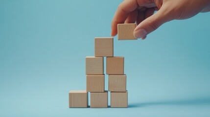 Obraz premium Transitioning into the year 2025, a hand adjusts wooden blocks on a soft blue backdrop, ideal for conveying growth and planning. Text space provided.