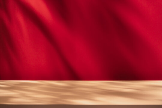Empty table on bright pink wall background. Composition with leaves shadow on red the wall and beige table. Mock up for presentation, branding products, cosmetics, food or jewelry.	