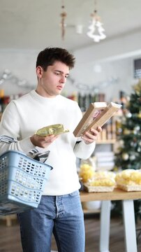 While shopping on eve of New Year holidays, young man buys sweets for festive party. Buyer examines packages with sweet dessert snacks, purchases chocolates and panellets, nougat.
