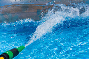 Fast flowing water from a garden hose fills up an inflatable paddling pool on a bright sunny day in...