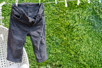 A pair of faded black denim, half-length shorts hang on a washing line.