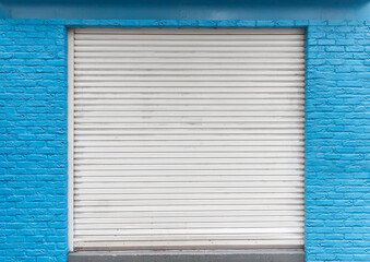 White closed steel shutter door and blue brick wall of warehouse, storefront for door background...