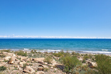 Stone coast of southern shore of big lake Issyk-Kul, summer vacation in Kyrgyzstan. Clear blue sky, emerald colored water of pond, small wave. Kirgiziya travel destination
