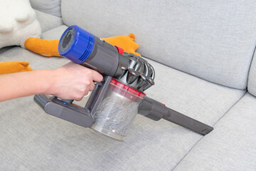 A woman cleans a sofa with a special portable vacuum cleaner for furniture