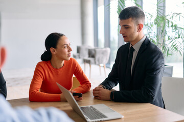 A young, diverse business team sitting together in a modern office, exchanging ideas and business plans, fostering collaboration and innovation for future success.