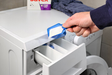 Close-up of a hand man pouring white washing powder into a washing machine. Housework in the...