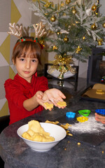 little girl makes xmas coockies with xmas decorations on the background