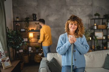 Portrait of adult woman stand and clean living room with broom
