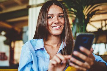 Portrait of happy cheerful hipster girl smiling and looking at camera while holding smartphone...