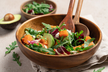 Sweet potato salad with arugula, avocado, cucumber and veta cheese in wooden bowl on light background. Healthy food top view. Food background with copy space