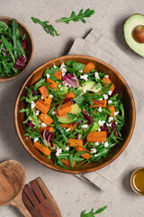 Sweet potato salad with arugula, avocado, cucumber and veta cheese in wooden bowl on light background. Healthy food top view. Food background with copy space